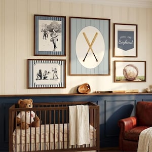 Op de afbeelding: Een galerijmuur met vijf ingelijste prints met honkbalthema's, waaronder illustraties van spelers, gekruiste knuppels, een honkbal en een bord met de tekst Long Live Boyhood. Onder de muur staat een houten wieg met een teddybeer in honkbaltenue.