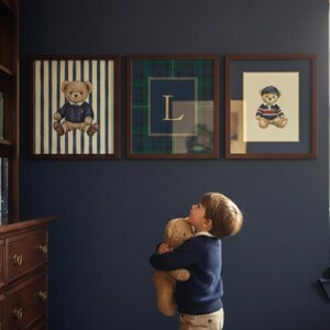 May include: Three framed pictures with teddy bear illustrations hang on a dark blue wall. The frames are brown. One picture has a teddy bear on a striped background, another has a plaid pattern with the letter "L", and the third has a teddy bear in a sailor outfit.