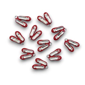 May include: A scattering of small, red ballet slipper charms with silver-coloured detailing. Each charm has a detailed design and a small loop for attaching to jewellery or crafts. The charms are arranged on a white background.