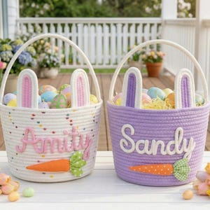 May include: Two Easter baskets, one white and one purple, each with bunny ears and filled with colorful eggs. The white basket has the name "Amity" and an orange carrot. The purple basket has the name "Sandy" and an orange carrot.