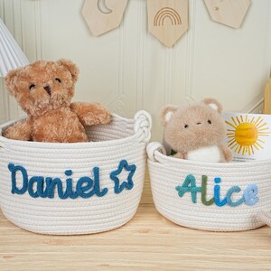 May include: Two white rope baskets with handles, each containing a stuffed bear. One basket has "Daniel" in blue script, the other "Alice" in blue and green. A children's book and a toy bunny are also visible.