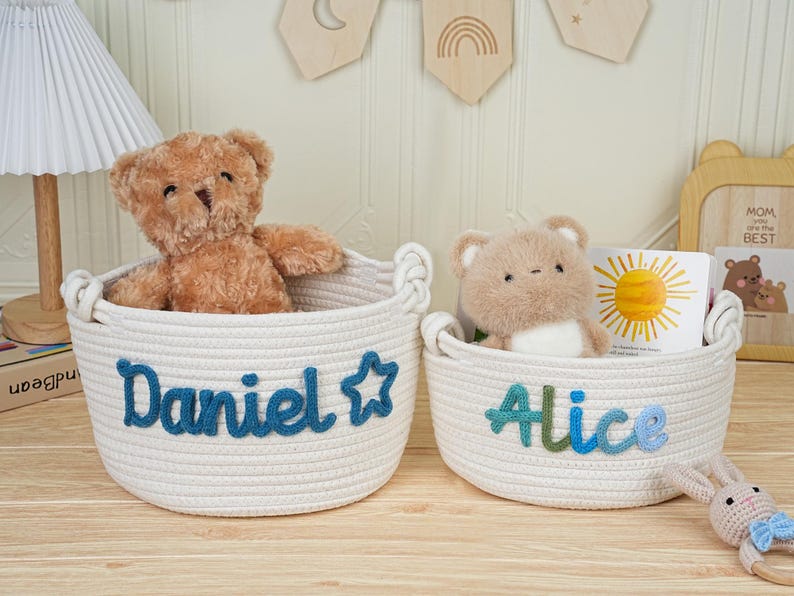 May include: Two white rope baskets with handles, each containing a stuffed bear. One basket has "Daniel" in blue script, the other "Alice" in blue and green. A children's book and a toy bunny are also visible.
