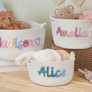 May include: Three white rope baskets with embroidered names: "Madison", "Amelia", and "Alice". Each basket contains a stuffed animal. The "Madison" basket has a teddy bear, the "Amelia" basket has a teddy bear and a pink blanket, and the "Alice" basket has a stuffed bunny.