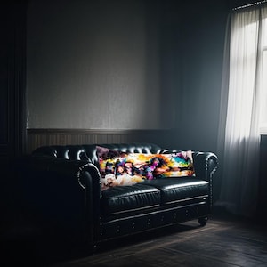 May include: A black leather sofa with a rectangular body pillow featuring abstract art. The pillow displays a vibrant mix of colours, including purple, yellow, and blue. The room has dark walls and a window with sheer curtains.