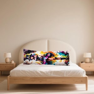 May include: A long, rectangular body pillow with a colourful abstract design. The artwork features a figure with vibrant splashes of yellow, blue, purple, and orange. The pillow is placed on a bed with a white comforter and wooden frame.
