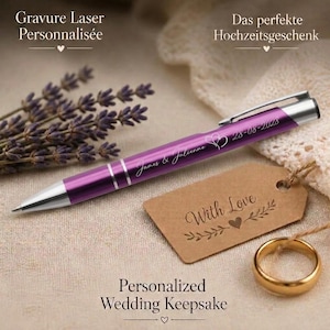 May include: A metallic purple ballpoint pen with silver accents, engraved with the names James & Julienne and the date 28-08-2028. A brown rectangular paper tag with the text With Love and a gold-toned metal ring are positioned nearby.