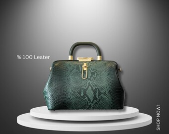 May include: A dark green leather handbag with a gold-toned clasp and a snakeskin pattern. The bag is sitting on a white platform.