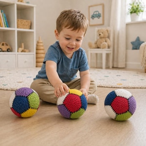 Peut inclure: Trois balles crochetées colorées avec des motifs géométriques. Les balles présentent une combinaison de rouge, jaune, bleu, vert, violet et blanc. Les balles sont sur un sol en bois de couleur claire. Un jeune enfant joue avec les balles.