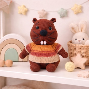 May include: A handmade brown crochet beaver doll with a striped orange, red, and tan sweater. The beaver has black eyes, a black nose, and two white teeth. A yellow ball and wooden star are nearby. A white bunny is in a basket.