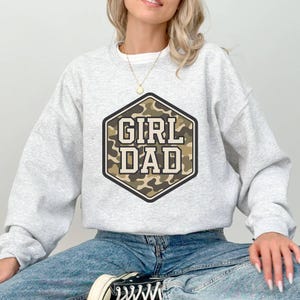 a woman sitting on the ground wearing a grey sweatshirt