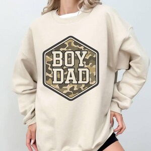 a woman wearing a sweatshirt with the words boy dad printed on it