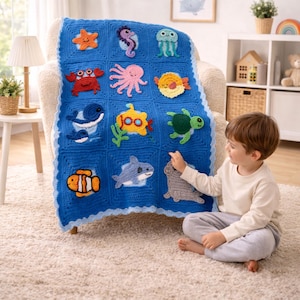 May include: A blue crochet blanket featuring various sea creatures, including a starfish, seahorse, jellyfish, crab, octopus, fish, whale, submarine, turtle, clownfish, shark, and seal. The blanket is draped over a chair.