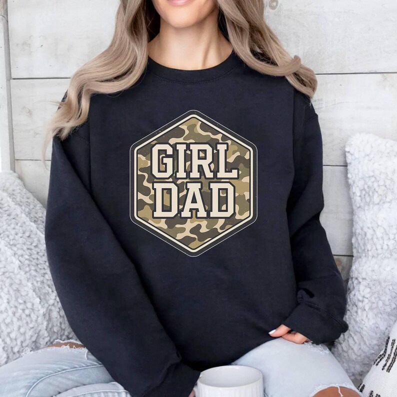 a woman sitting on a bed wearing a black sweatshirt that says girl dad