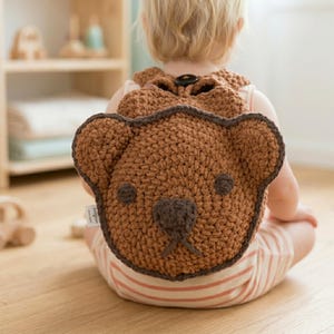 May include: A brown crochet backpack shaped like a teddy bear, with dark brown accents around the edges and features. The backpack is worn by a child, with the focus on the bear-shaped design. The backpack has a button closure.