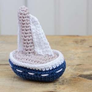 Peut inclure: Un jouet en forme de voilier crocheté avec une voile blanche et une coque bleue. Le jouet est fait de fil doux et est parfait pour la salle de jeux d'un enfant.