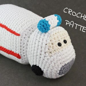 May include: White crocheted ambulance toy with red stripes, blue and white striped siren, and black eyes. Crochet pattern.
