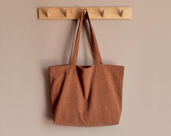 May include: A rust-colored corduroy tote bag with two shoulder straps, hanging from a light-colored wooden wall hook rack. The text DinastyUA is visible above the hook rack. The bag features a vertical ribbed texture and a simple rectangular shape.