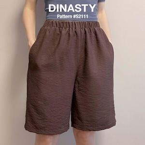 Puede incluir: Pantalones cortos de color marrón oscuro con cintura elástica y acabado de tela texturizada. Los pantalones tienen bolsillos laterales y se combinan con una parte superior azul. El texto DINASTY y Pattern #S2111 están impresos en blanco.