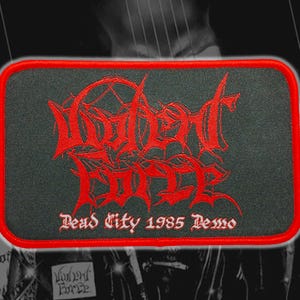 Könnte beinhalten: Rechteckiger, gestickter Aufnäher mit den Worten "Violent Force" in roter gotischer Schrift auf schwarzem Hintergrund. Der Aufnäher hat einen roten Rand und den Text "Dead City 1985 Demo" unter dem Haupttext.