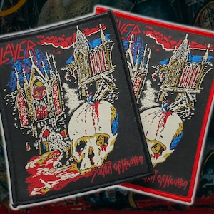 May include: Two rectangular embroidered patches featuring the Slayer logo and the text South of Heaven. The design depicts a gothic cathedral, a skull with a sword, and red blood splatters on a black background with a stitched border.