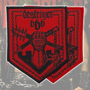 Pode incluir: Dois patches vermelhos e pretos com o texto "destroyer 666" e um gráfico de uma manopla com espinhos e armas cruzadas. Os patches têm uma borda de corrente e são provavelmente para uma jaqueta ou bolsa.