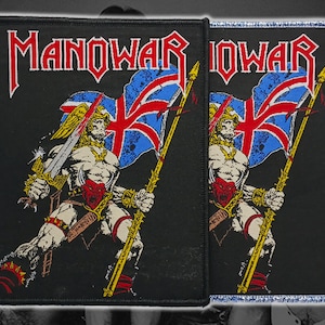Peut inclure: Écusson rectangulaire noir avec le nom du groupe "MANOWAR" en rouge et blanc. L'écusson représente un guerrier musclé tenant une épée et un drapeau Union Jack. Le guerrier porte une armure dorée et rouge.