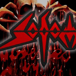 Könnte beinhalten: Ein roter und schwarzer Aufnäher mit dem Wort "SODOM" in einer stilisierten Schriftart. Der Aufnäher hat einen schwarzen Rand und ist vor einem dunklen, abstrakten Hintergrund mit roten und orangen Farbtönen platziert.