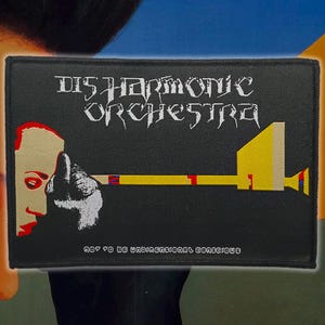 May include: Black rectangular patch with the text "DISHARMONIC ORCHESTRA" in white gothic font. The patch features a graphic of a face and a yellow and red trumpet. The text "NOT TO BE UNIDIMENSIONAL CONSCIOUS" is at the bottom.