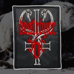 May include: Black embroidered patch with the word "DESTROYER" in red, featuring a cross and the number "666". The patch has a white border and two snake-like figures at the top. The background is a blurred image of a wolf.