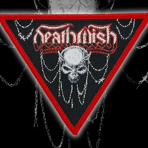 May include: A black, triangular patch with a red border. The patch features the word "Deathwish" in white, stylized lettering above a white skull with horns. Chains and decorative elements surround the skull.