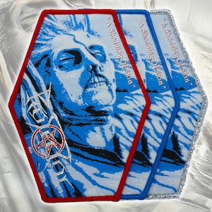 Pode incluir: Três emblemas bordados hexagonais com um gráfico azul e branco de um rosto, o texto "A Shedding Of Skin" e um símbolo de pentagrama vermelho. Os emblemas têm bordas costuradas em vermelho, azul e prata, respectivamente, com fios detalhados.