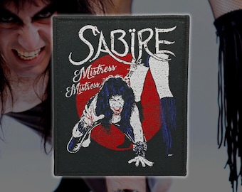 May include: A rectangular black fabric patch featuring white embroidered text that reads Sabire and Mistress Mistress. The design includes a central red circle with a white graphic of a person with long dark hair crawling forward.
