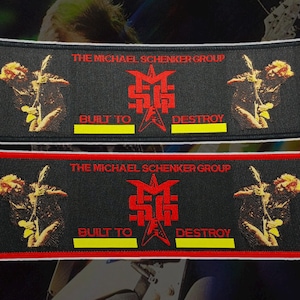 Pode incluir: Dois patches retangulares com fundos pretos. O patch superior tem uma borda branca e o inferior uma borda vermelha. Ambos os patches apresentam o texto "THE MICHAEL SCHENKER GROUP" e "BUILT TO DESTROY" em vermelho e amarelo.