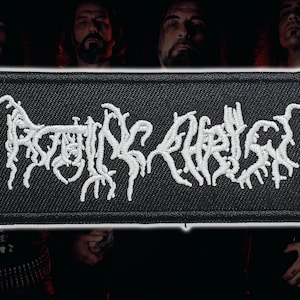 May include: A rectangular black embroidered patch featuring the white text Rotting Christ in a stylized, jagged, and branch-like font. The patch has a thick black stitched border and a textured fabric surface, showcasing detailed white thread work.