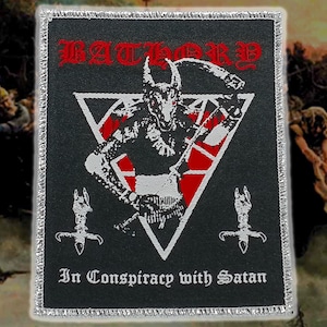 Könnte beinhalten: Schwarzer Aufnäher mit dem Wort "BATHORY" in roter gotischer Schrift. Ein weißes umgekehrtes Dreieck enthält eine gehörnte Figur mit einer Sense. Der Text "In Conspiracy with Satan" steht darunter. Silberner Rand.