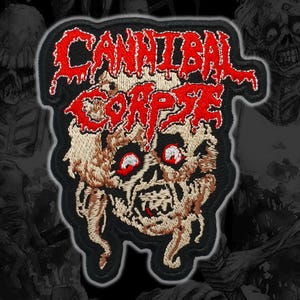 May include: An embroidered patch featuring the text CANNIBAL CORPSE in a dripping red font above a detailed, beige-toned skull illustration with prominent red eyes and exposed teeth, all set against a solid black background with a dark border.