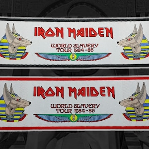 May include: Embroidered patch featuring the Iron Maiden logo and the text "World Slavery Tour 1984-85." The patch includes Anubis imagery and a winged design. Available with a black or red border.