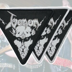 以下が含まれることがあります： バンドVenomの白い刺繍ロゴと様式化されたヤギの頭のグラフィックが施された、3枚の三角形の黒い布製パッチ。各パッチにはステッチが施された縁取りがあり、鋭く角張ったフォントでVenomという文字がデザインされています。