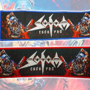 Op de afbeelding: Twee rechthoekige geborduurde patches met het Sodom bandlogo en de tekst Code Red in zilverdraad. Het ontwerp bevat aan weerszijden een centrale afbeelding van een soldaat, tegen een zwarte achtergrond met rode accenten en een gekleurde rand.