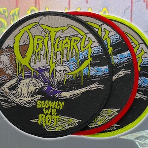 以下が含まれることがあります： ネオン・グリーンで「Obituary」というバンド名が書かれた3つの丸いパッチ。朽ち果てた姿が描かれています。パッチは黒い背景に赤と黄色の縁取りがあり、「Slowly We Rot」という文字が書かれています。