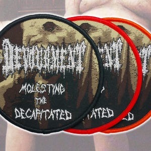 May include: Three circular embroidered patches featuring the text Devourment and Molesting the Decapitated in a jagged white font. The patches have a dark brown and black background with a central graphic and are bordered in black, red, and orange.