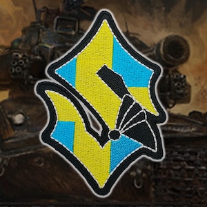 Könnte beinhalten: Gestickter Aufnäher mit einem stilisierten Design in Gelb, Hellblau und Schwarz, mit weißem Rand. Der Aufnäher hat eine einzigartige Form und ist vor einem verschwommenen Hintergrund eines Militärpanzers platziert.