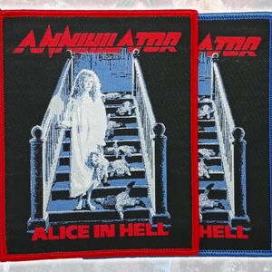 May include: Two rectangular embroidered patches featuring the Annihilator Alice in Hell album cover art. The design shows a person in a white gown on a staircase with dolls, with red text reading Annihilator and Alice in Hell on a black background.
