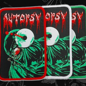May include: Rectangular patches with a black background, featuring the word "AUTOPSY" in dripping red letters. The patches depict a green figure with a white eye and a red dot. Each patch has a different colored border: red, white, and green.
