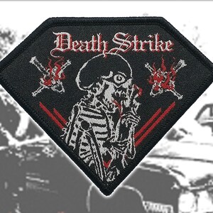 Puede incluir: Un parche bordado en forma de diamante con fondo negro. Presenta un gráfico de esqueleto blanco con un motivo de llamas rojas y el texto "Death Strike" en una fuente blanca estilizada. El diseño incluye dos objetos cruzados con llamas rojas.