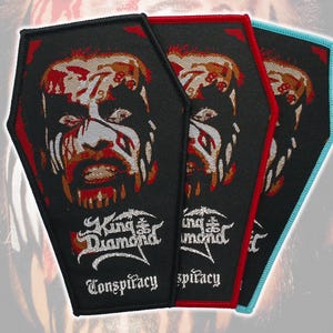 May include: Three coffin-shaped embroidered patches featuring the face of King Diamond with white face paint and red accents. Each patch displays the text King Diamond and Conspiracy in white embroidery, with borders in black, red, and light blue.