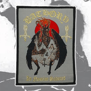 May include: A rectangular embroidered patch with a gray background and black border. It features a central Baphomet figure with black wings, a red sun, and gold text reading Bathory and In Nomine Satanas, with two inverted gold crosses on the sides.