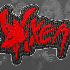 Może przedstawiać: Czarna haftowana naszywka z napisem Vixen wykonanym stylizowaną, poszarpaną czerwoną czcionką. Projekt zawiera czerwoną sylwetkę głowy lisa zintegrowaną z pierwszą literą, z grubą czarną obwódką otaczającą cały czerwony kształt graficzny.