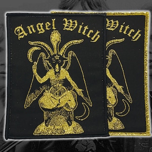 May include: Two black patches with gold embroidered text and imagery. The text reads "Angel Witch" in an ornate font. The image is of a horned figure with wings. One patch has a gold border.