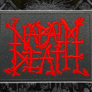 Puede incluir: Parche rectangular con las palabras "SLAM DEATH" bordadas en rojo brillante sobre un fondo gris oscuro. El texto tiene una fuente estilizada y dentada. El parche tiene un borde gris.